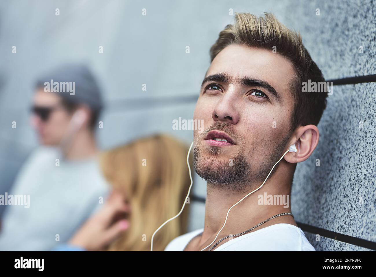 Giovani adolescenti che ascoltano musica sullo stesso paio di cuffie, vestiti con abiti eleganti sullo sfondo di una g Foto Stock