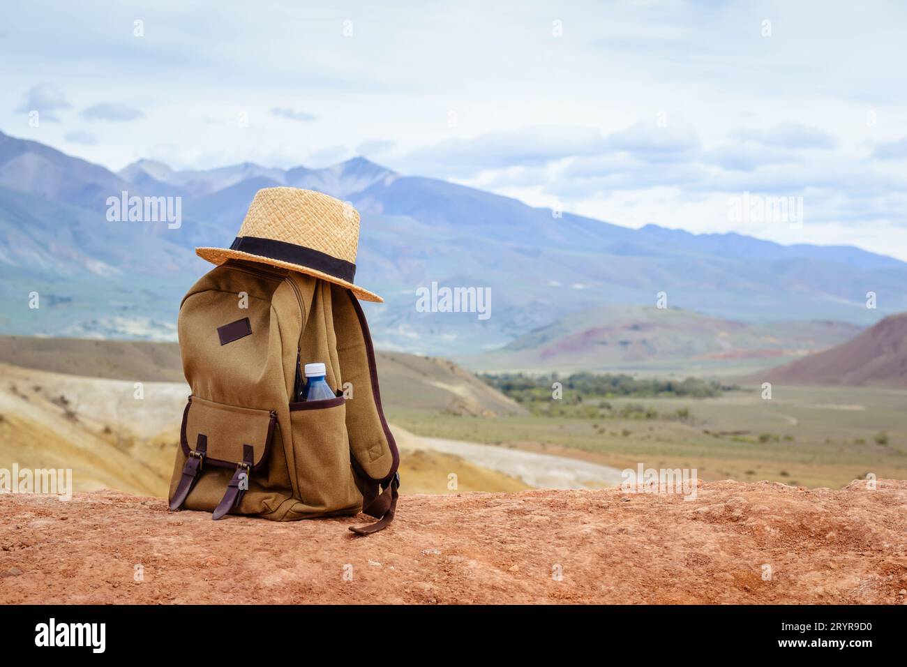 Zaino hipster, bottiglia d'acqua e cappello di paglia sulla collina sullo sfondo delle montagne. Concetto di marcia attiva. Foto Stock