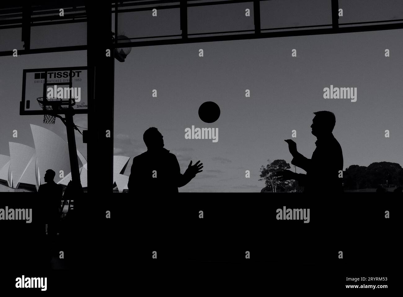 Uomini con silhouette che lanciano un pallacanestro Sydney Opera House visti "incorniciati" dalla sala OSPT Cargo e da un canestro da basket americano Foto Stock