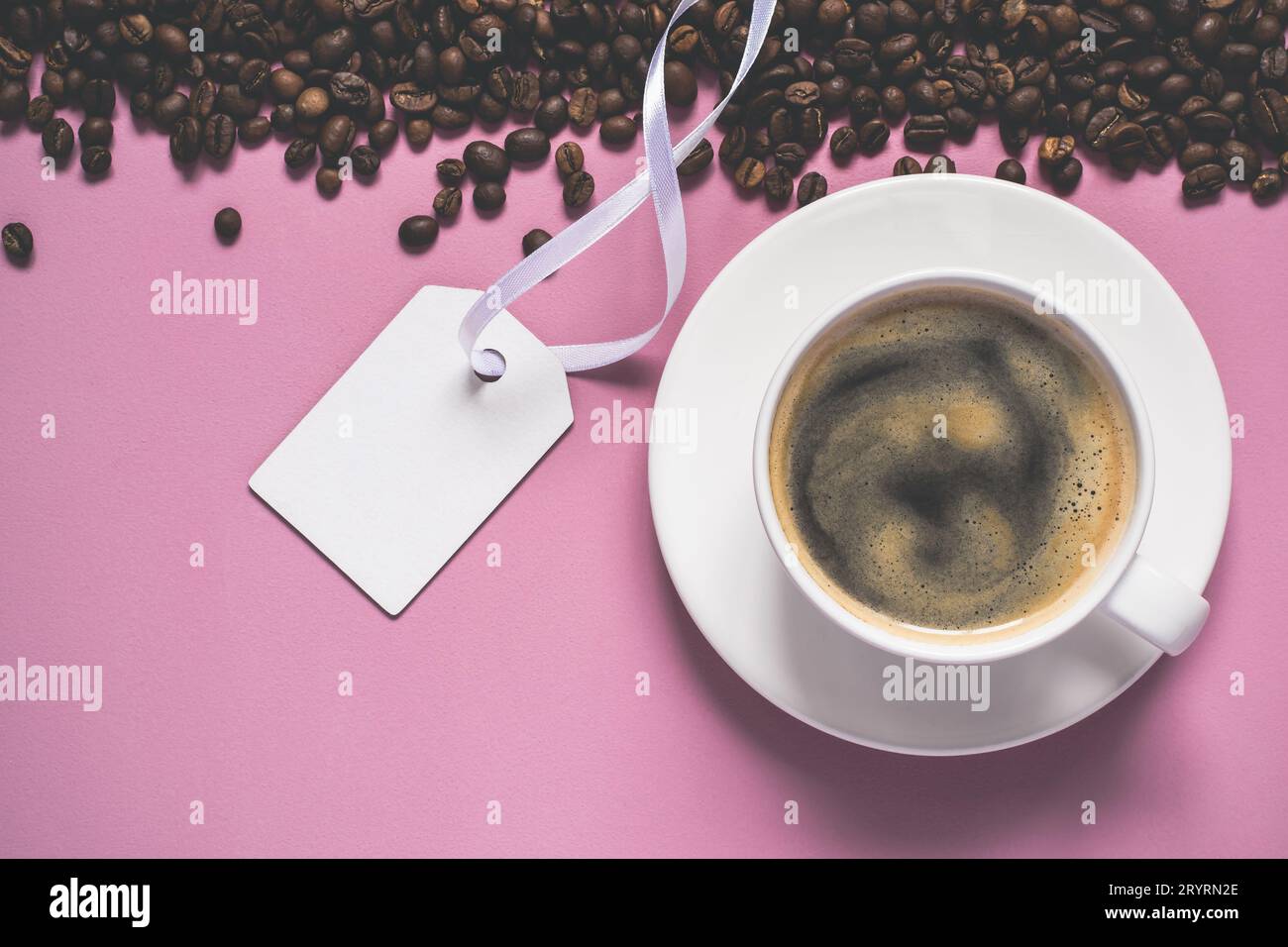 Tazza di caffè con schiuma, chicchi e cartellino su sfondo rosa Foto Stock