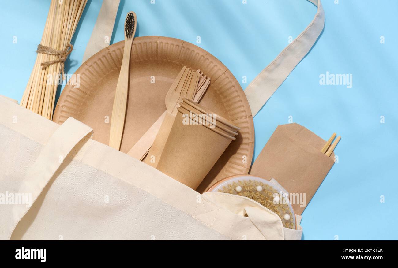 Borsa in cotone bianco, forchette in legno, piatti e tazze su sfondo blu. Concetto di riciclaggio dei rifiuti, zero rifiuti Foto Stock