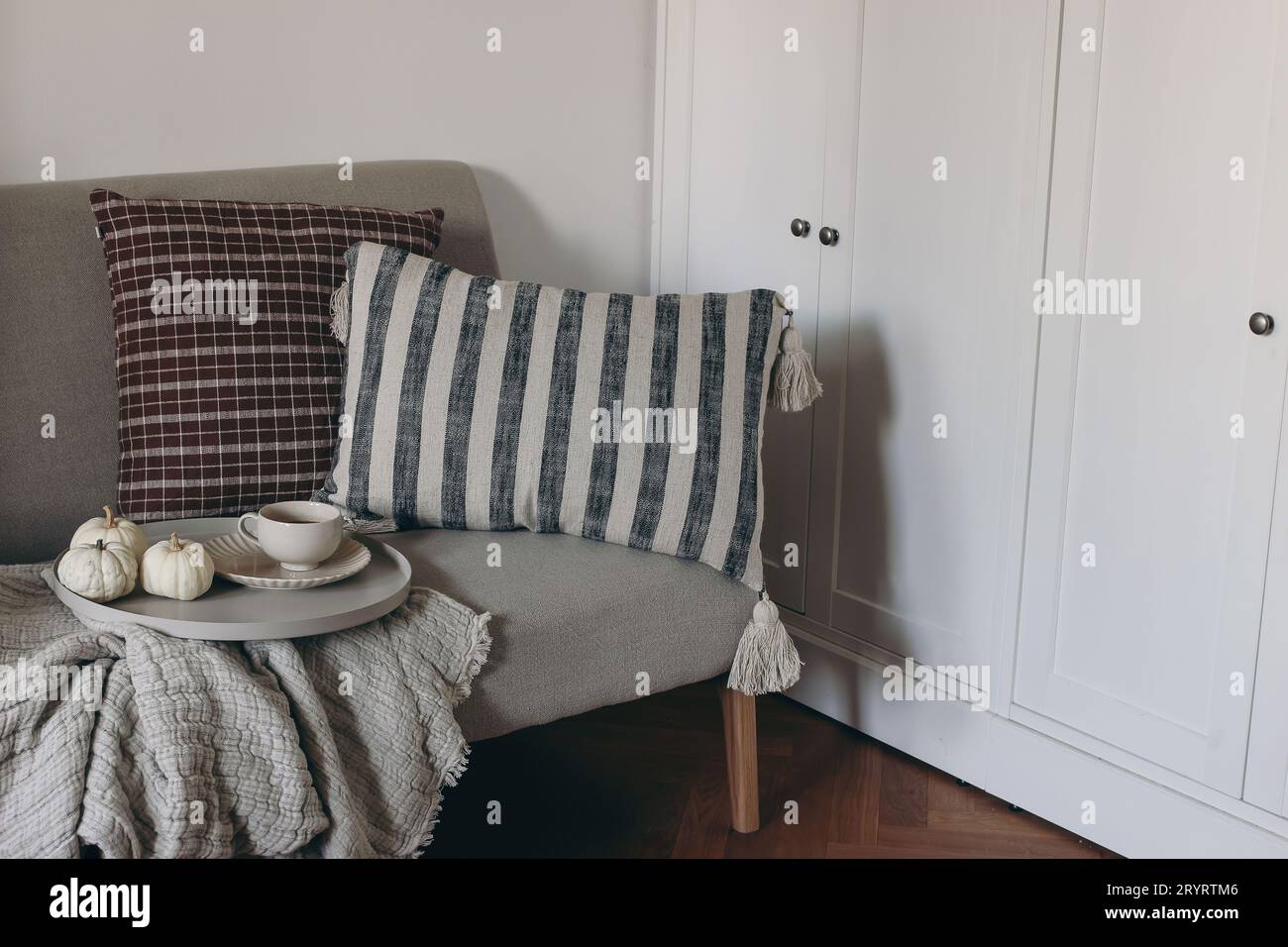 Soggiorno autunnale natura morta. Tazza di caffè, tè su vassoio rotondo Piccole zucche bianche. Colazione con divano in lino, cuscini a righe a scacchi Foto Stock