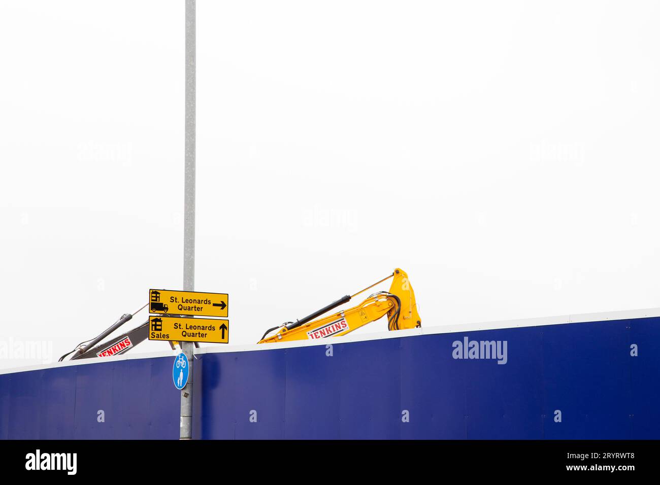 Nuovo sviluppo a St. Leonards Exeter - segnaletica gialla per St. Vendite trimestrali Leonards, con sollevatore a forchetta giallo coordinato dietro una parete barriera blu Foto Stock