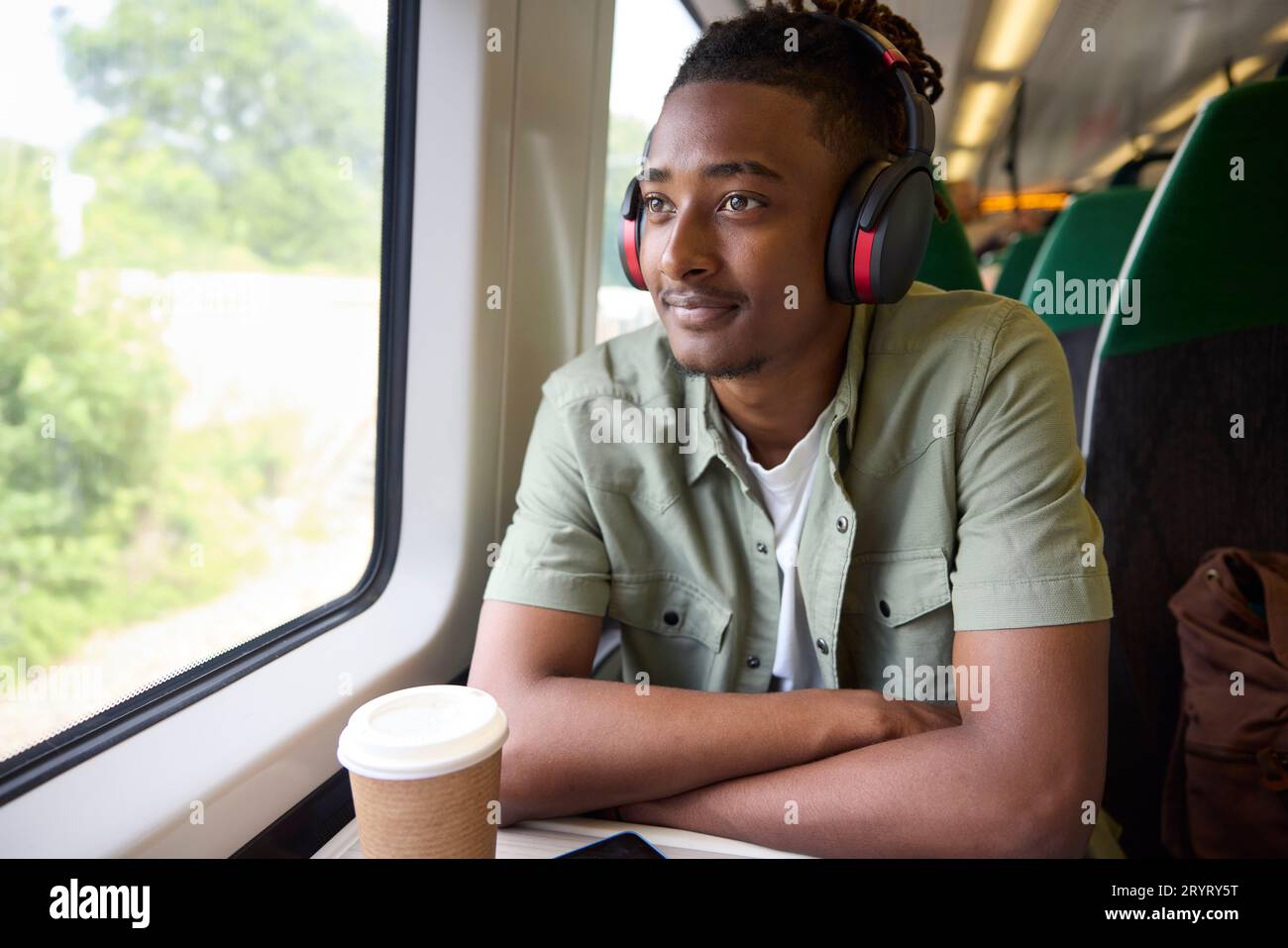Giovane che viaggia per lavoro seduto sul treno e indossa cuffie wireless Foto Stock