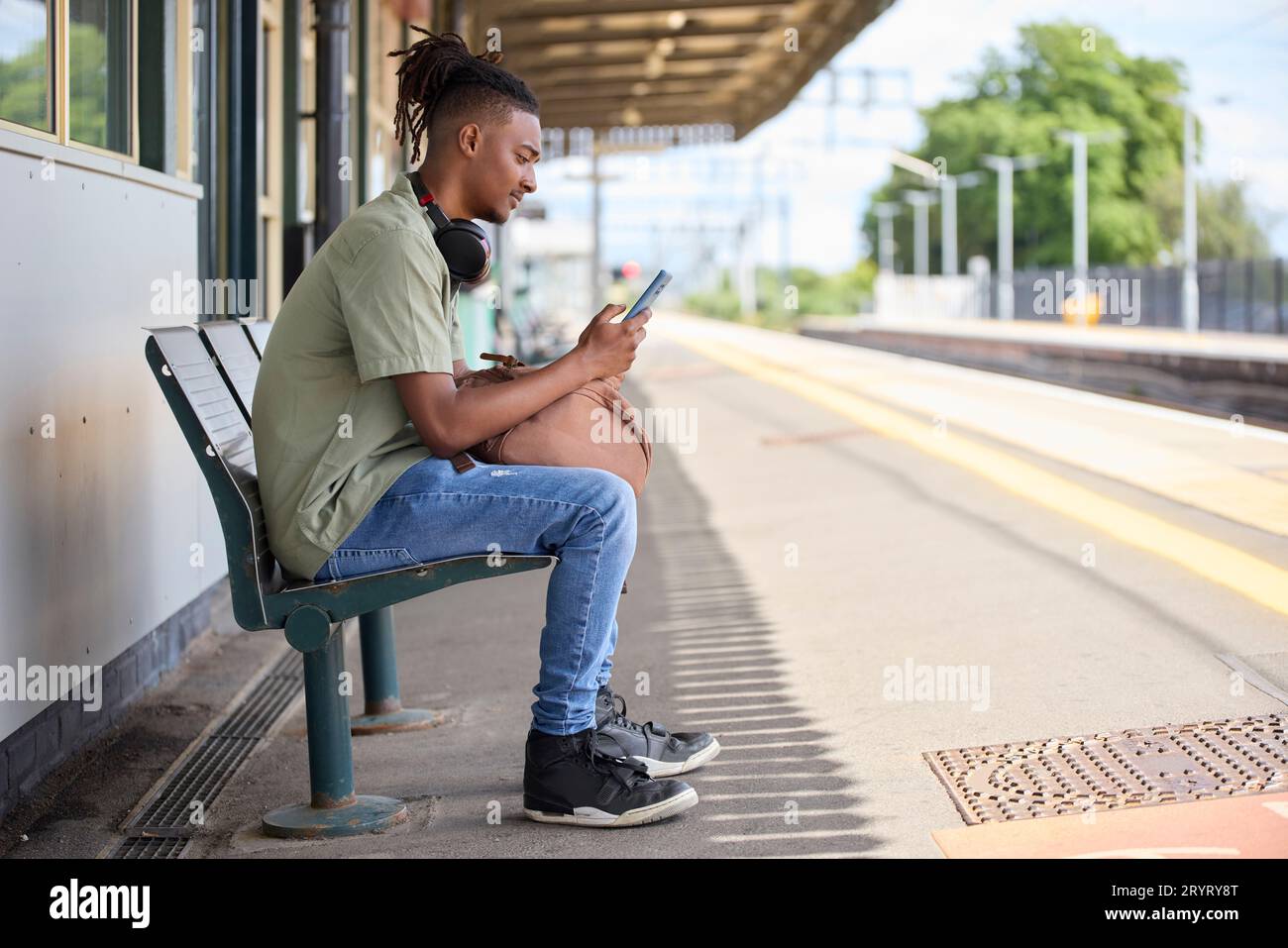 Giovane che viaggia per lavoro in treno seduto sulla piattaforma guardando un telefono cellulare per informazioni di viaggio o social media Foto Stock
