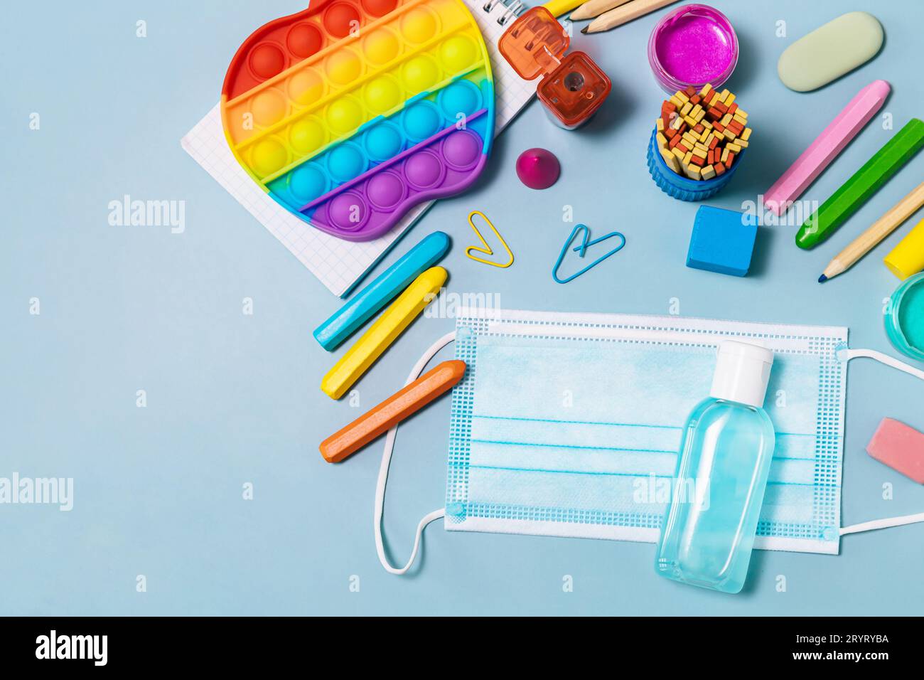 Forniture scolastiche, antistress, maschera facciale, bottiglia di igienizzatore, per tornare a scuola su sfondo blu. Precautio COVID-19 Foto Stock