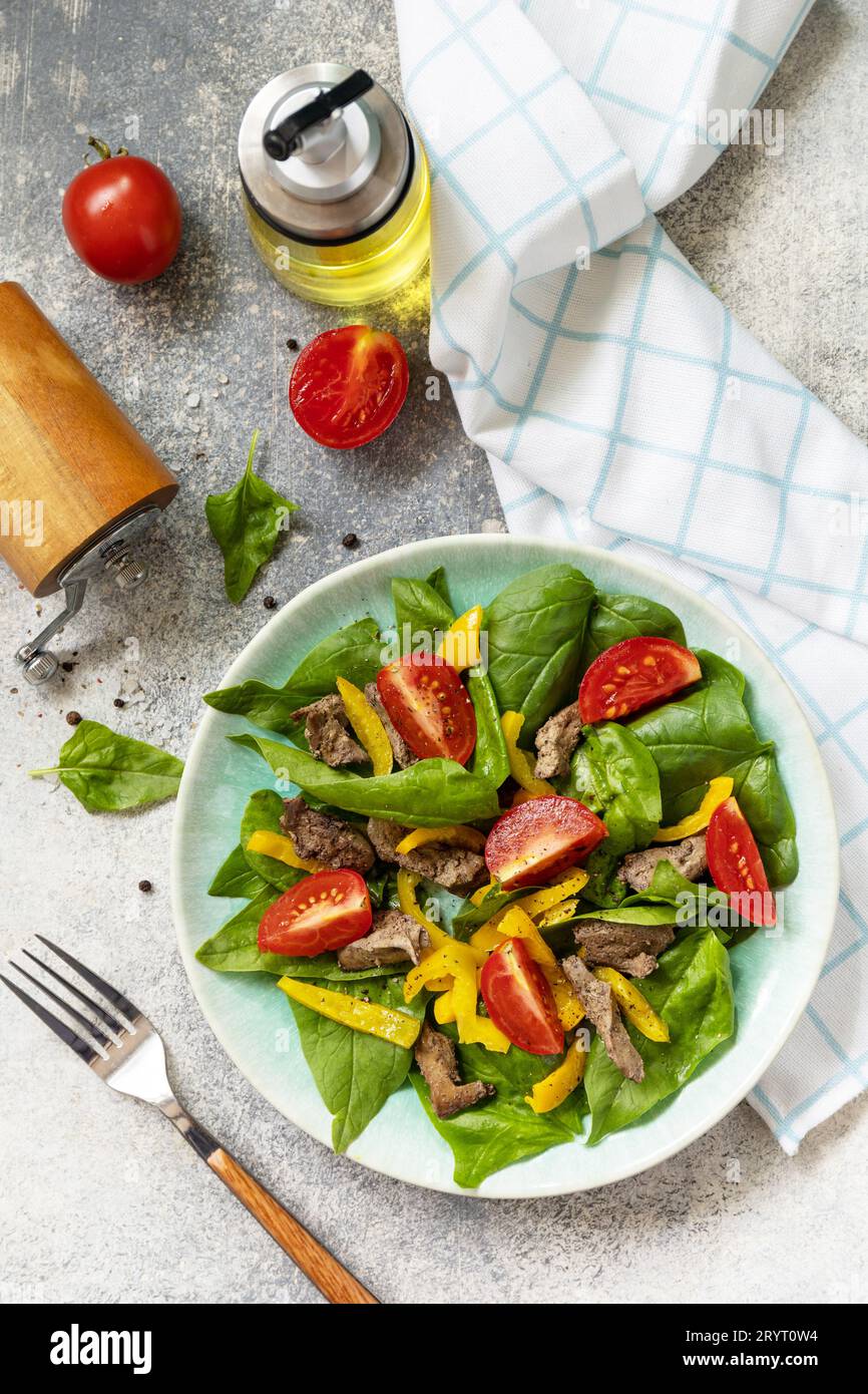 Insalata calda di spinaci giovani, fegato di pollo, pomodori e peperoni grigliati con spezie e aceto balsamico. Dieta keto sana a basso contenuto di carboidrati. V Foto Stock