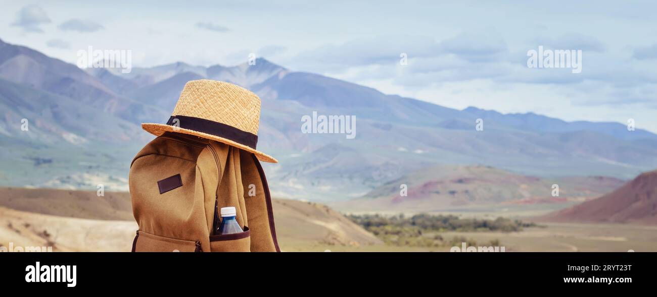Hipster zaino, bottiglia di acqua e il cappello di paglia sulla collina sullo sfondo delle montagne. Attiva il concetto di viaggio Foto Stock