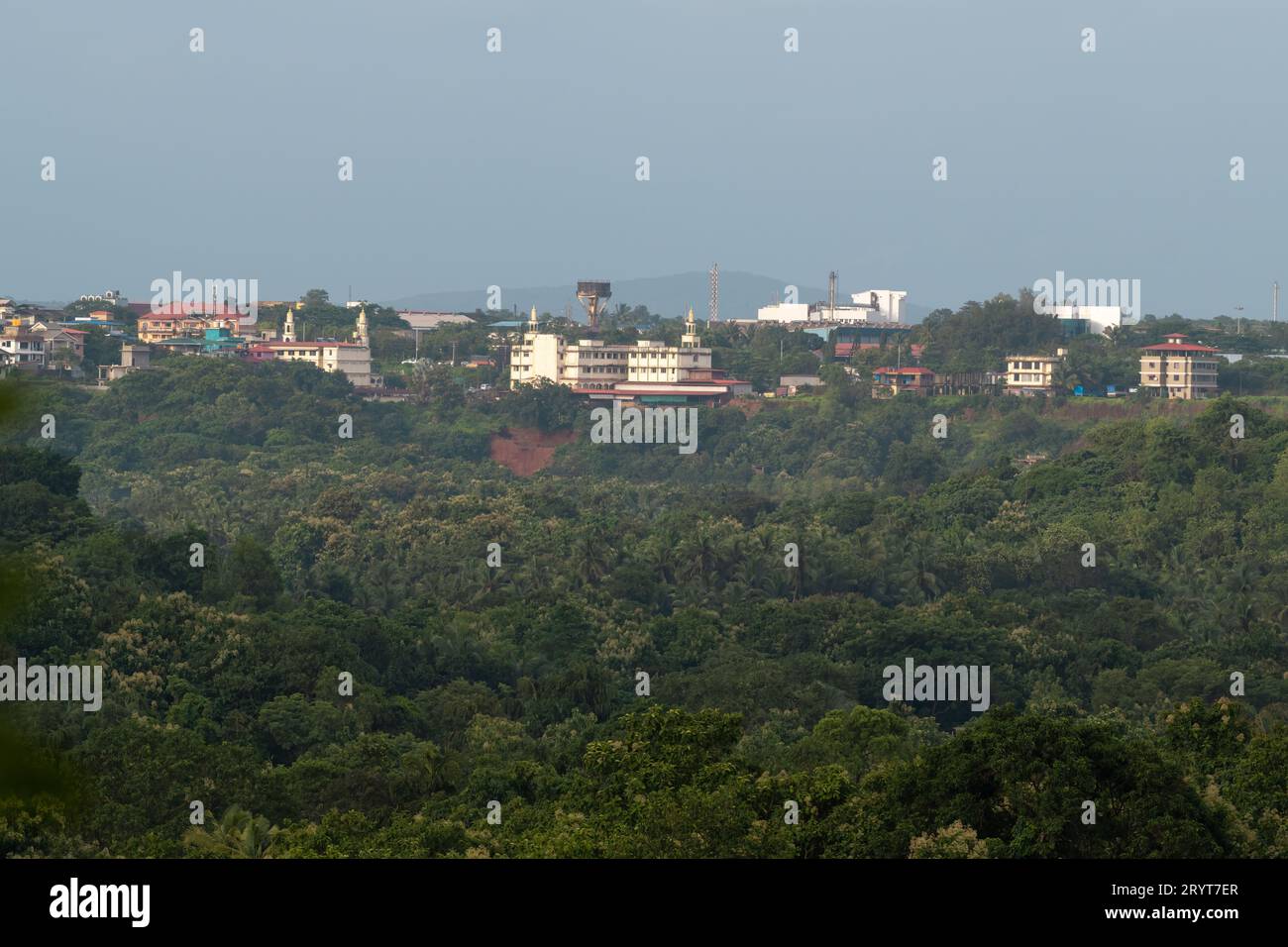 Vista della città industriale di Verna a distanza e circondata da una lussureggiante foresta pluviale nello stato di Goa, India. Foto Stock