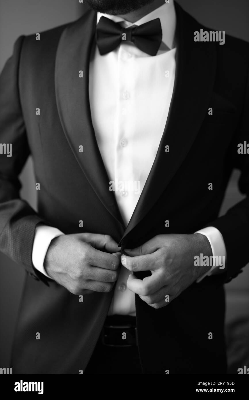 Un giovane adulto che indossa uno smoking formale, che regola la cravatta nera nello specchio, preparandosi per un evento speciale Foto Stock
