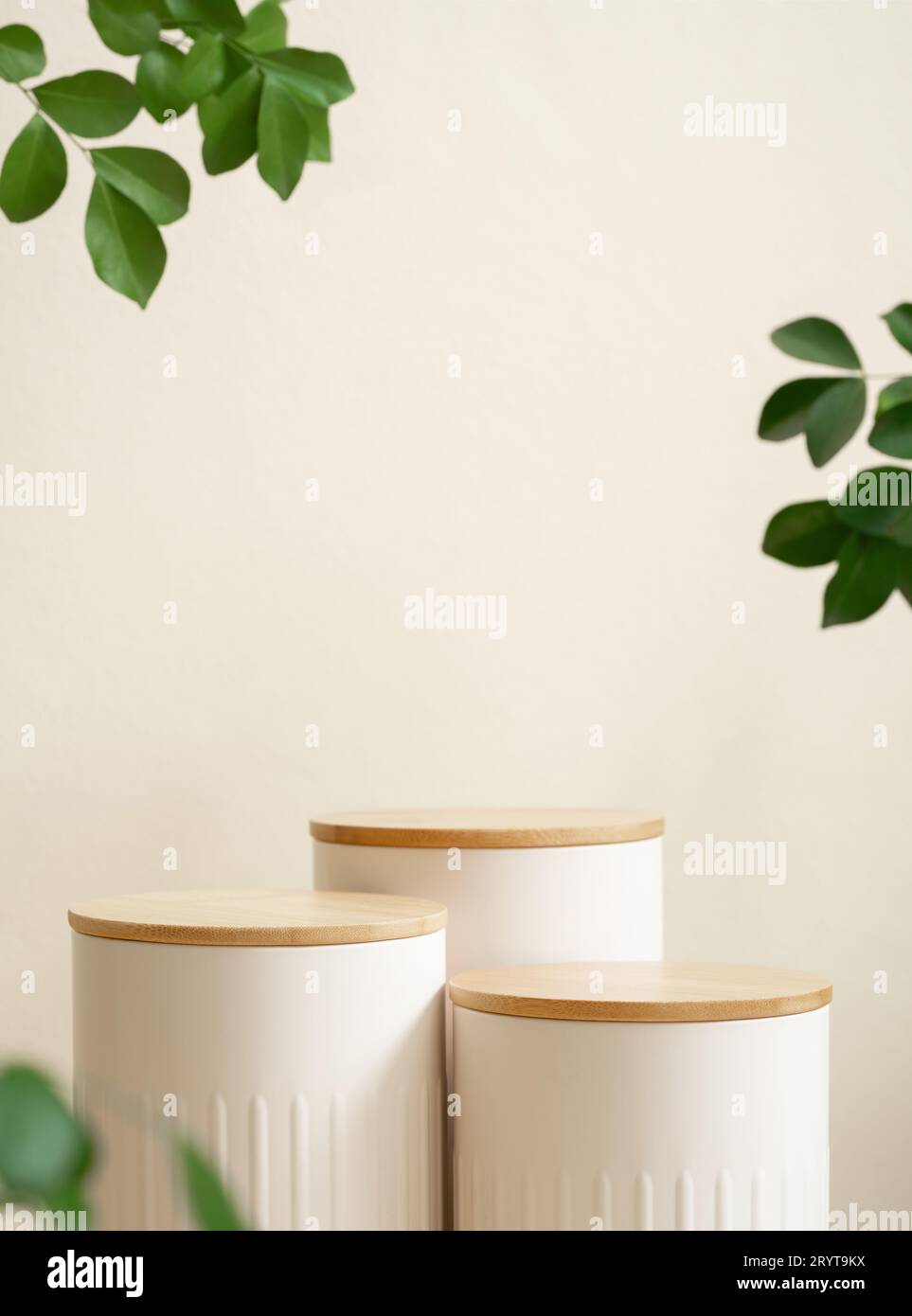 Podio bianco in legno minimale con piante di foglie verdi sfocate su sfondo beige. Cosmetici di bellezza, prodotti delicati naturali, display moderno, eco-compatibile con la natura Foto Stock