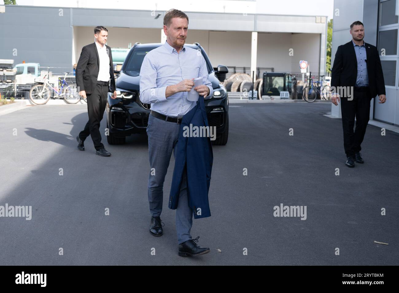 Dresda, Germania. 2 ottobre 2023. Michael Kretschmer (CDU), ministro presidente della Sassonia, si trova di fronte alla sua auto ufficiale durante la sua visita alla HolyPoly, una Start-up di riciclaggio con sede a Dresda. L'azienda sviluppa programmi di riciclaggio personalizzati per il recupero di materie plastiche monovarietà da rifiuti plastici misti. Credito: Sebastian Kahnert/dpa/Alamy Live News Foto Stock