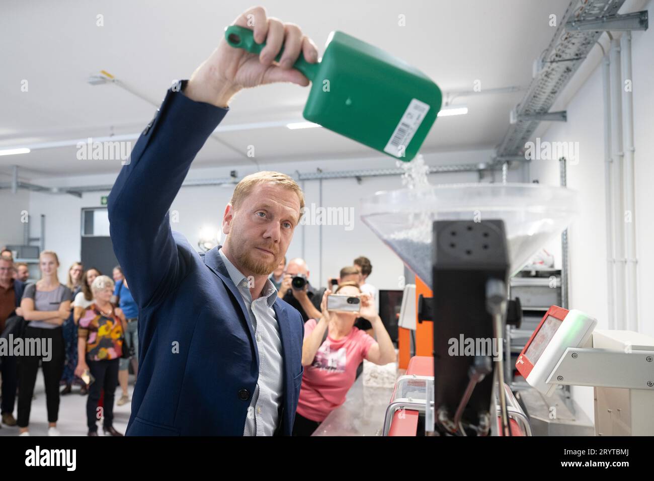 Dresda, Germania. 2 ottobre 2023. Michael Kretschmer (CDU), Ministro Presidente della Sassonia, scarica granuli di plastica nella tramoggia di una macchina per lo stampaggio ad iniezione durante la sua visita alla HolyPoly, una Start-up di riciclaggio con sede a Dresda. L'azienda sviluppa programmi di riciclaggio personalizzati per il recupero di materie plastiche monovarietà da rifiuti plastici misti. Credito: Sebastian Kahnert/dpa/Alamy Live News Foto Stock