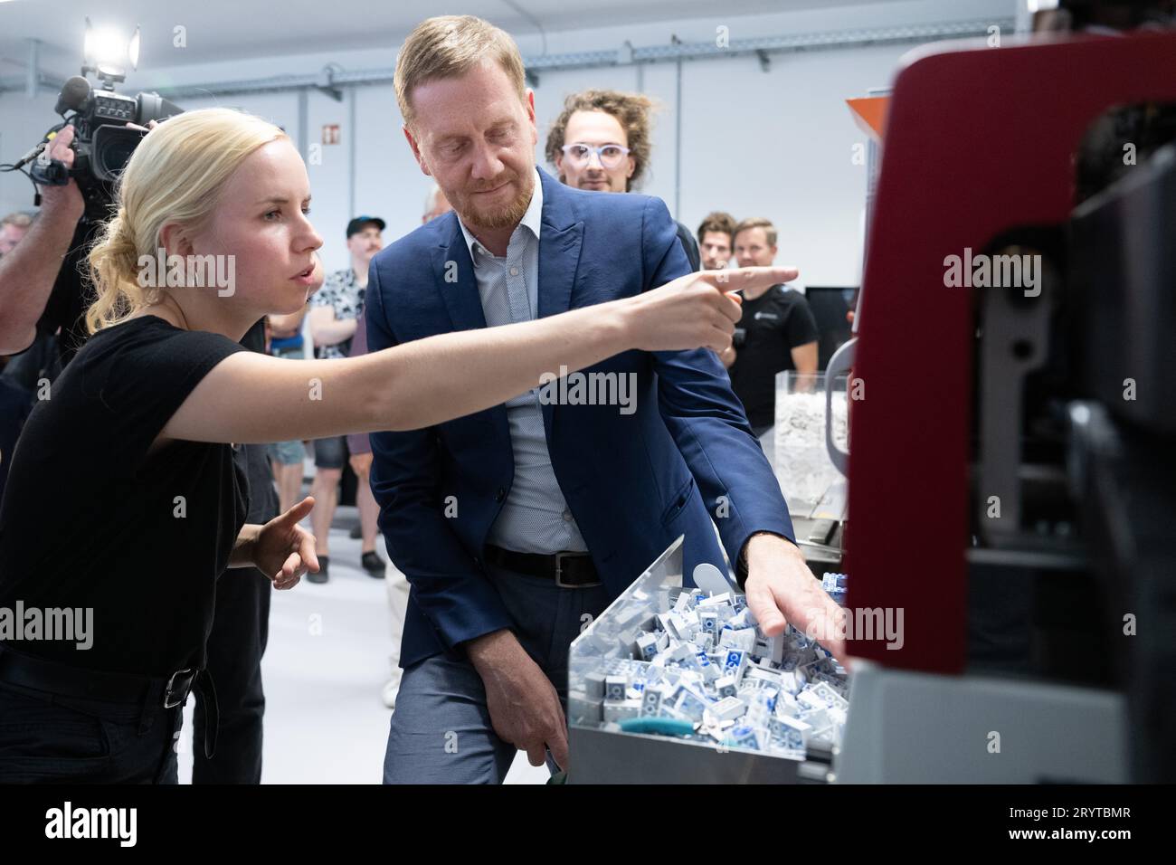 Dresda, Germania. 2 ottobre 2023. Michael Kretschmer (CDU), Ministro Presidente della Sassonia, si trova a una macchina per lo stampaggio ad iniezione con Dorothee Wendler, ingegnere delle materie plastiche, durante la sua visita alla HolyPoly, una Start-up di riciclaggio con sede a Dresda. L'azienda sviluppa programmi di riciclaggio personalizzati per il recupero di materie plastiche monovarietà da rifiuti plastici misti. Credito: Sebastian Kahnert/dpa/Alamy Live News Foto Stock