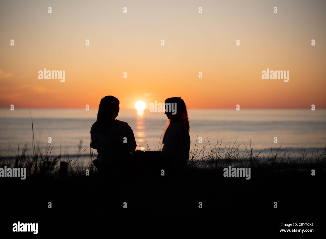 Le due amiche si godono una conversazione mentre guardano il tramonto su una spiaggia Foto Stock