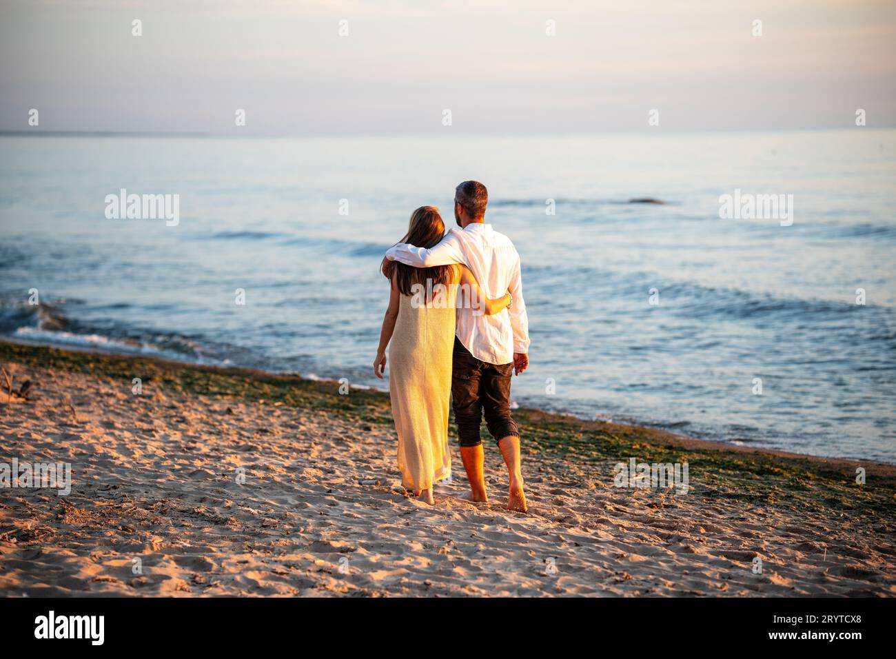 Una coppia attraente che cammina sulla spiaggia, sotto il cielo blu Foto Stock
