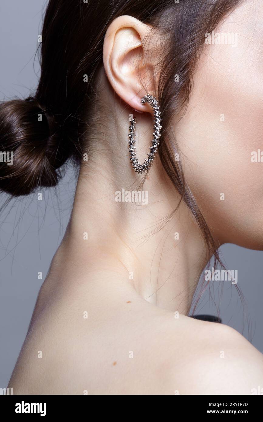 Vista laterale femminile Bunette con nodo di capelli e orecchino nell'orecchio su sfondo grÐµy. Foto Stock