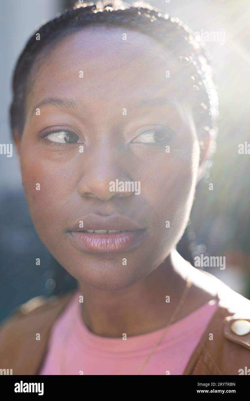 La luce del sole su una donna afroamericana che guarda lontano, in piedi fuori casa Foto Stock