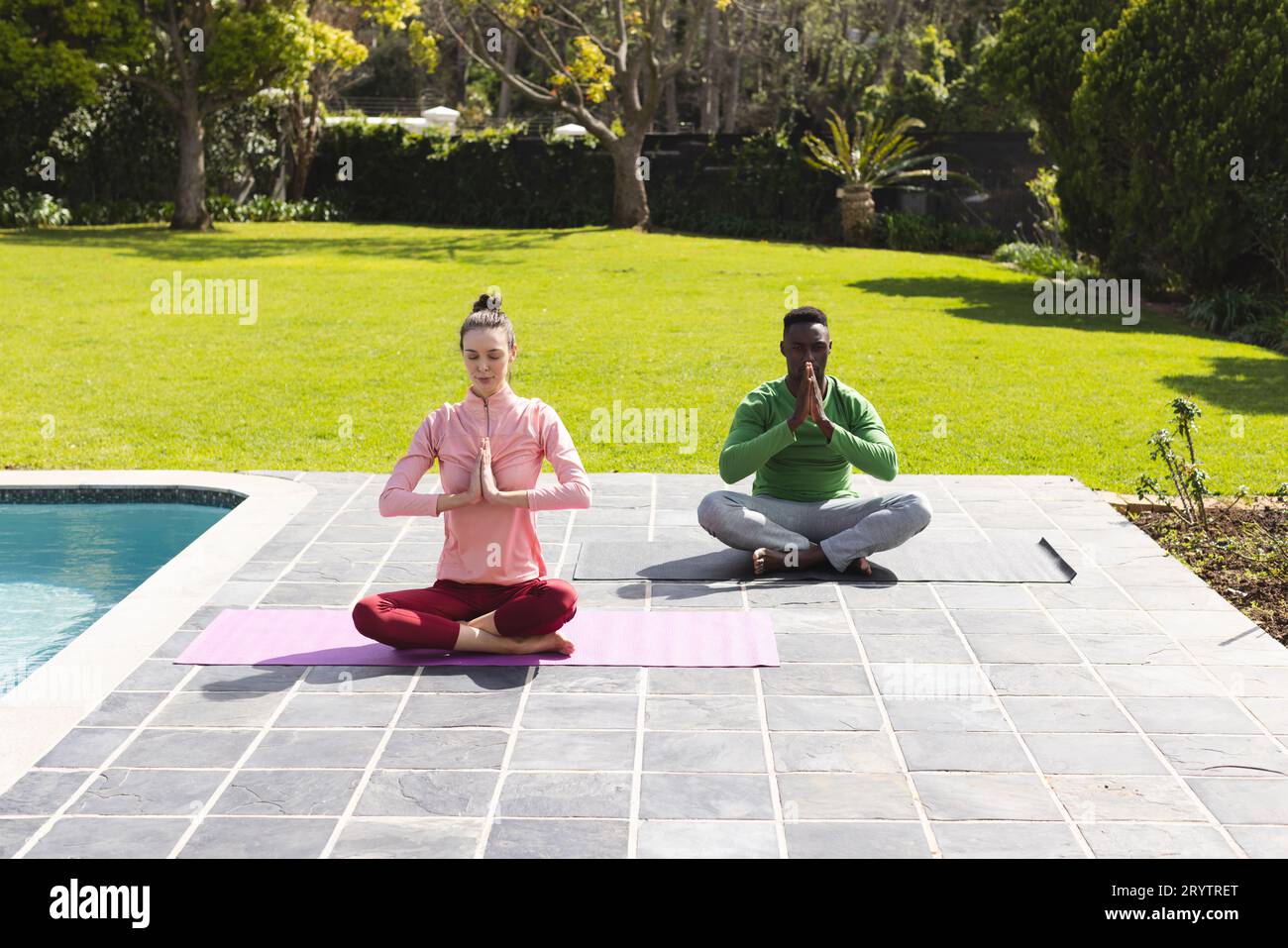 Coppie diverse che praticano yoga e meditano vicino alla piscina in giardino Foto Stock