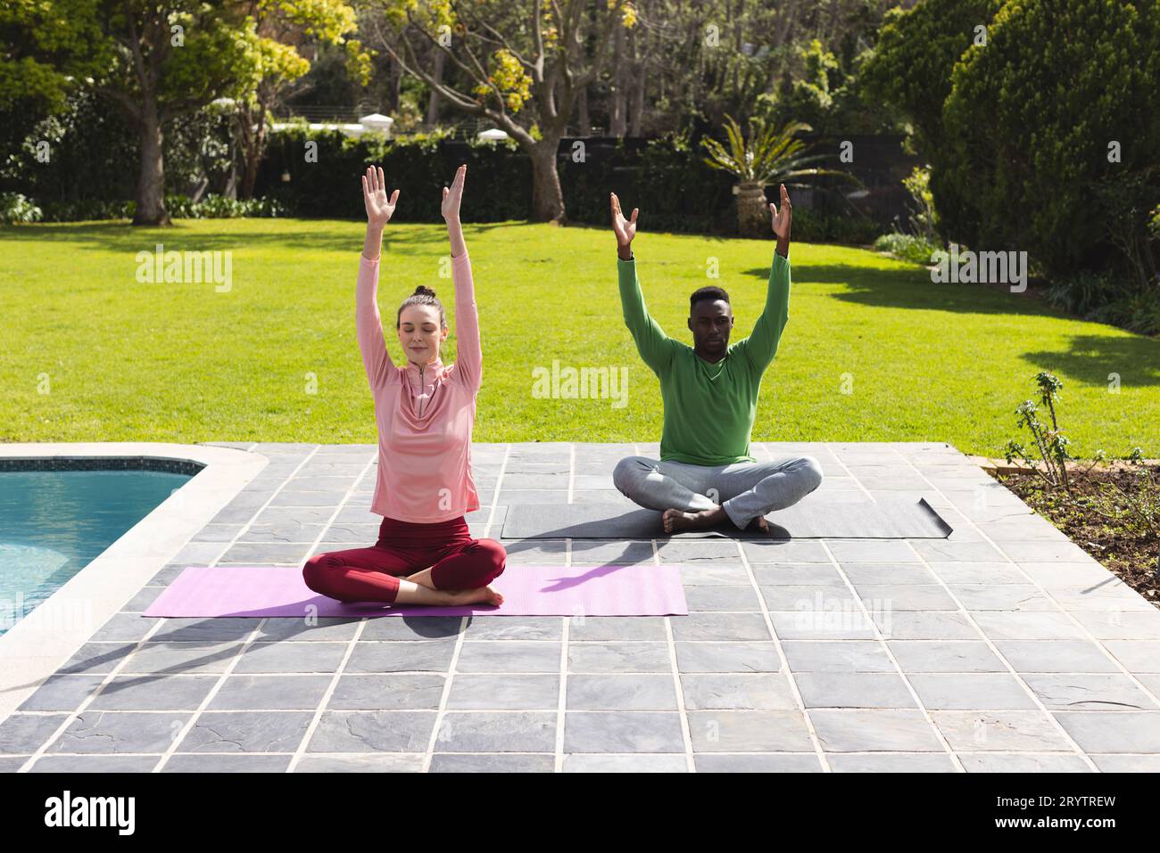 Coppie diverse che praticano yoga e meditano vicino alla piscina in giardino Foto Stock