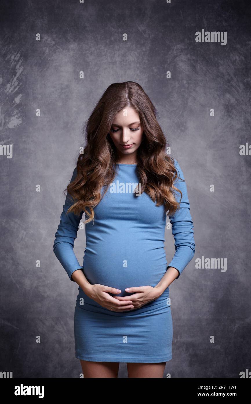 Ritratto di una giovane bella donna incinta in vestito blu. Donna con le mani vicino alla pancia incinta e sostiene lo stomaco con le mani Foto Stock