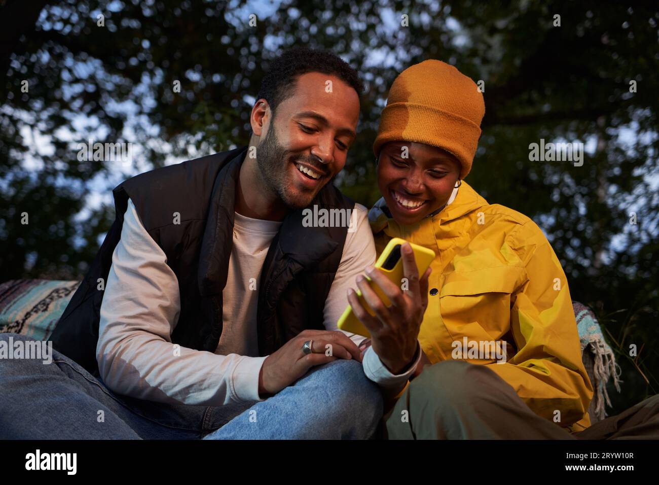 Felice giovane coppia afro-americana che usa mobili all'aperto. Due amici felici seduti che sembrano telefono. Foto Stock