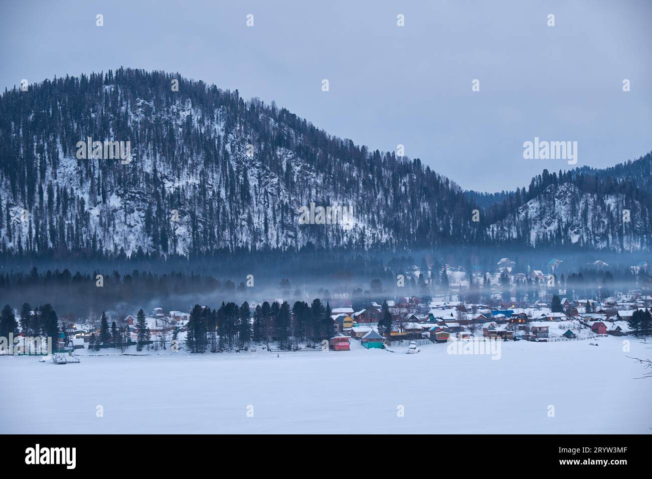 Case sulla riva del lago ghiacciato Teletskoe sotto il fumo del camino. Iogach, Altai. Foto Stock