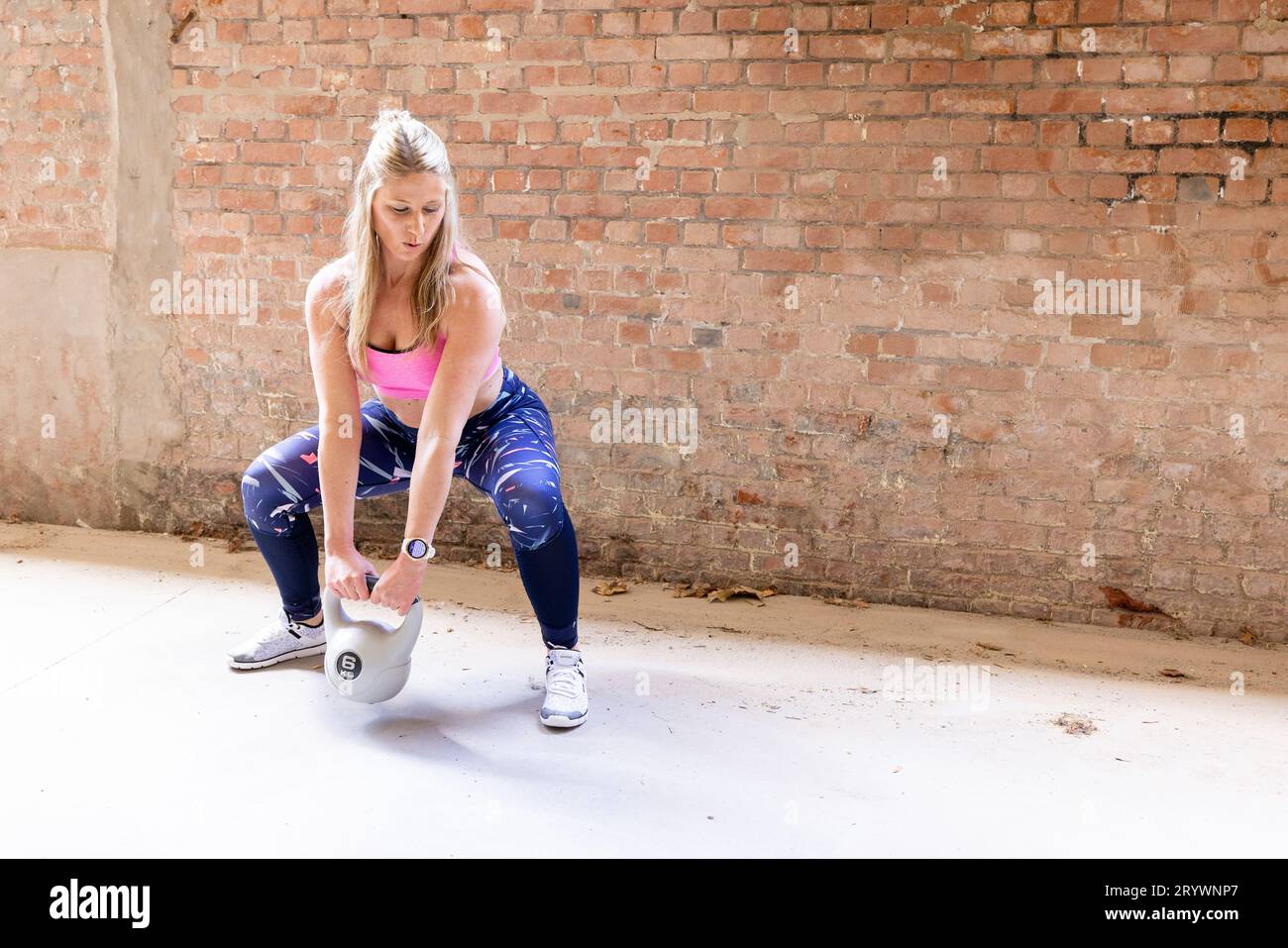 Giovane donna bionda che solleva il kettlebell pesante in ambiente fitness industriale Foto Stock