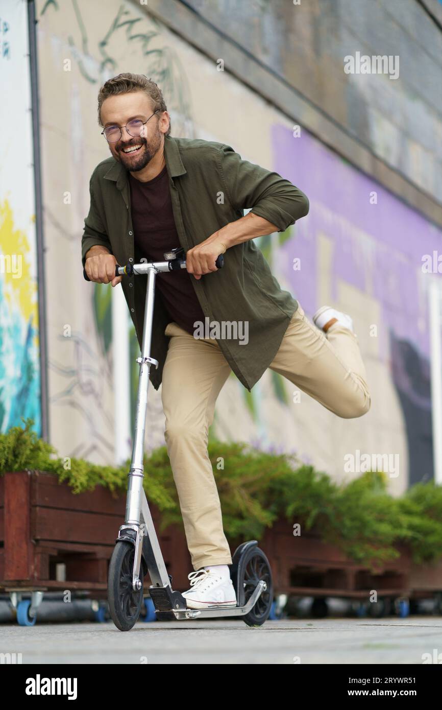 Vita divertente e felice come un uomo sorridente guida uno scooter per strada. Con un sorriso infuocato e un'espressione di pura gioia, egli imbalsama Foto Stock