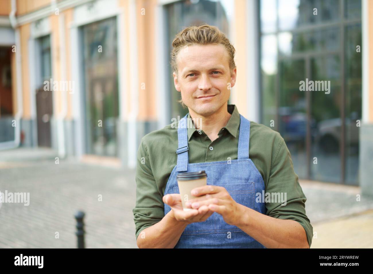 Concetto di caffè in movimento, in quanto il cameriere offre una tazza di caffè caldo al cliente in strada. Ospitalità urbana e convenienza Foto Stock