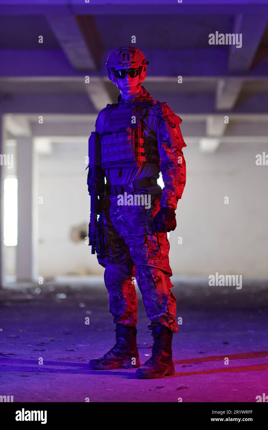 Un soldato professionista intraprende una pericolosa missione in un edificio abbandonato illuminato da luci blu e viola al neon Foto Stock