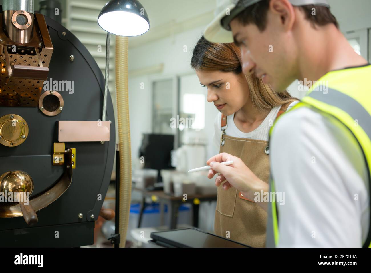 Ritratto di una giovane lavoratrice del magazzino che parla con un tecnico della macchina per torrefazione del caffè nella torrefazione del caffè Foto Stock
