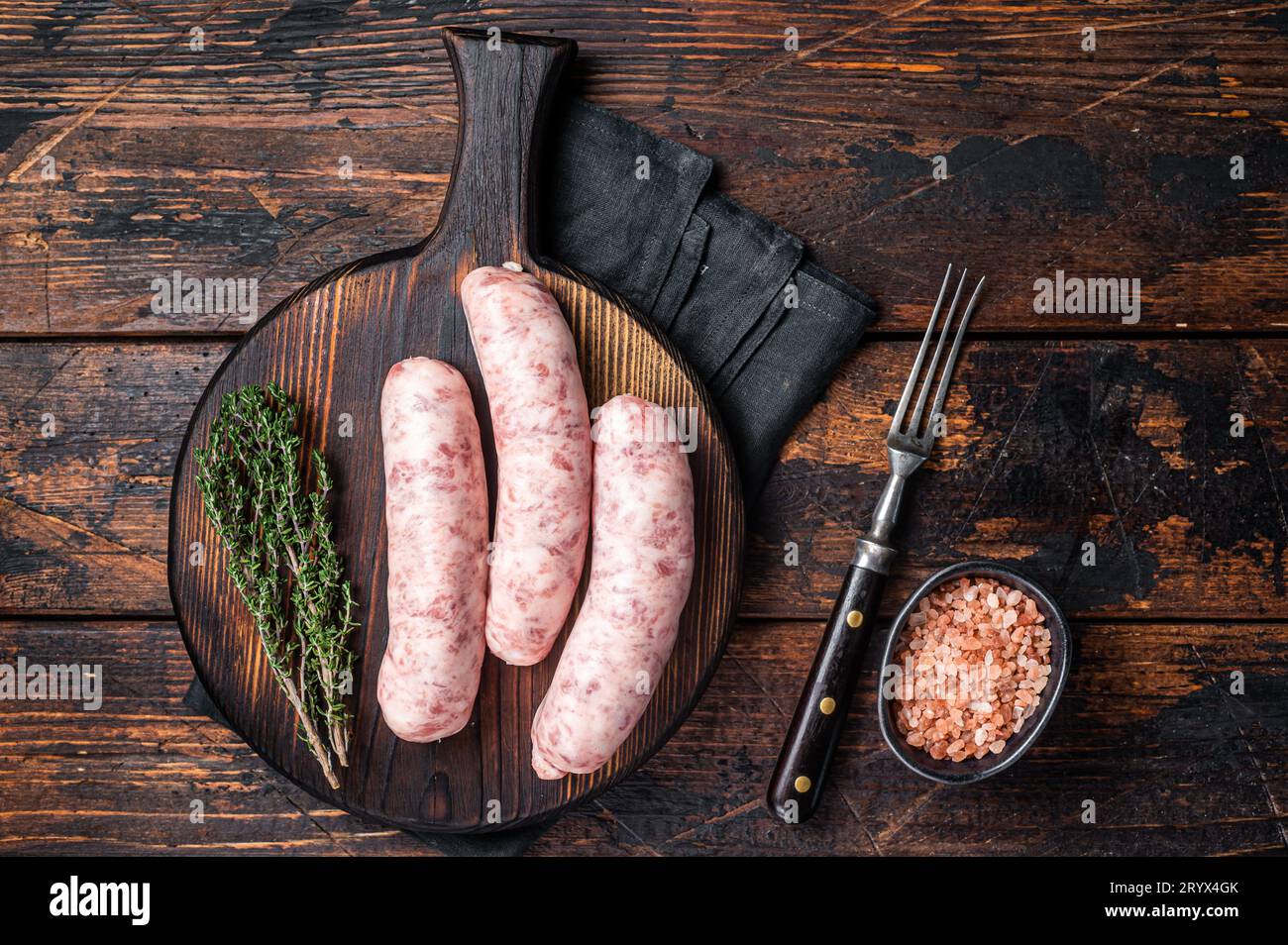 Salsicce di carne di Bratwurst crude fresche pronte per la cottura su asse di legno. Sfondo di legno. Vista dall'alto. Foto Stock