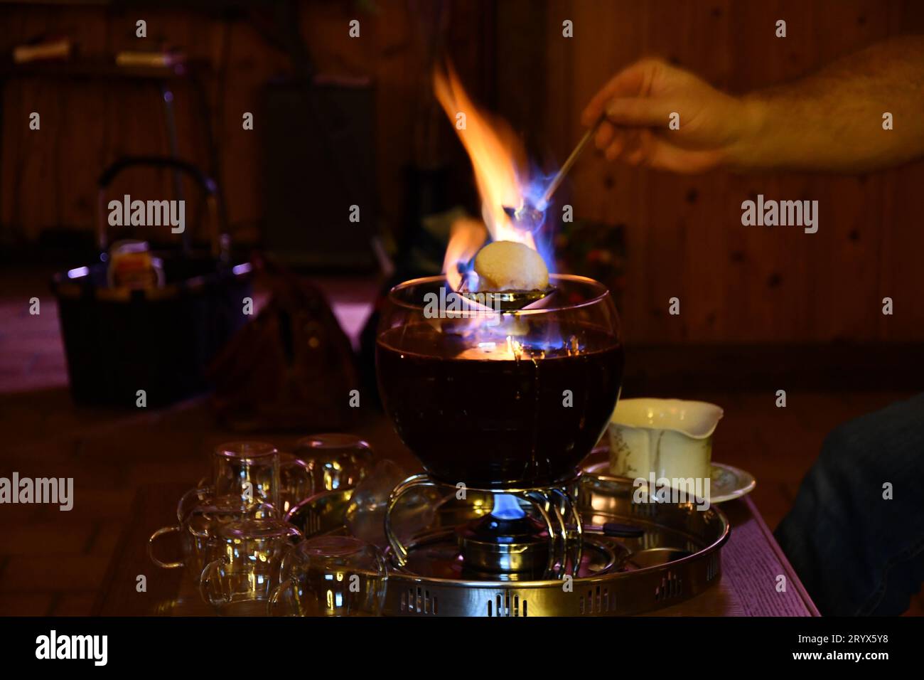 Cameriere che mette un pan di zucchero in fiamme su una ciotola di Feuerzangenbowle su un tavolo del ristorante Foto Stock