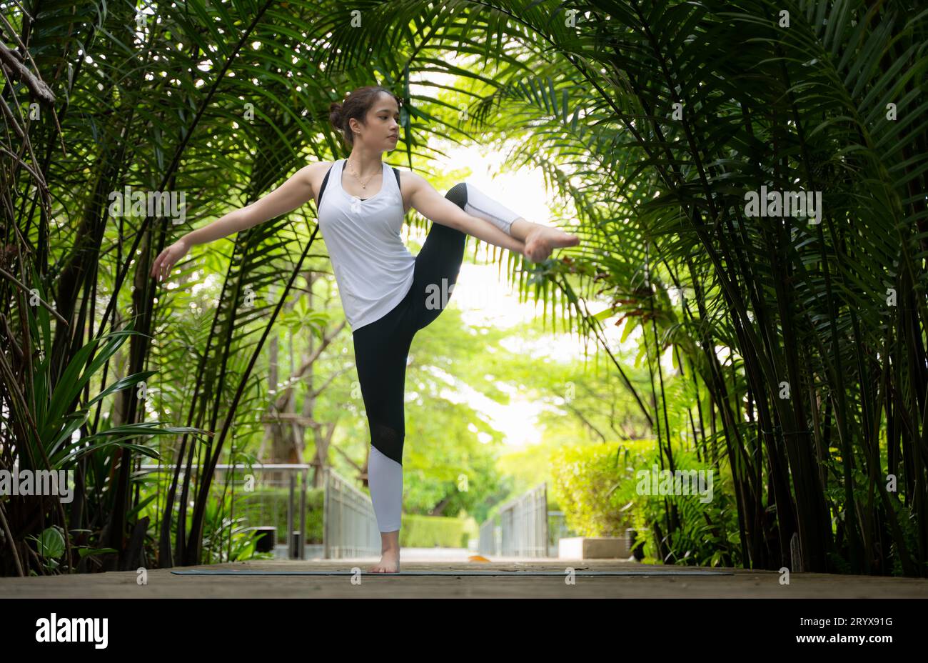 Giovane femmina nel giardino ci sono passerelle in legno e un tunnel di alberi verdi freschi, con attività yoga per la salute Foto Stock