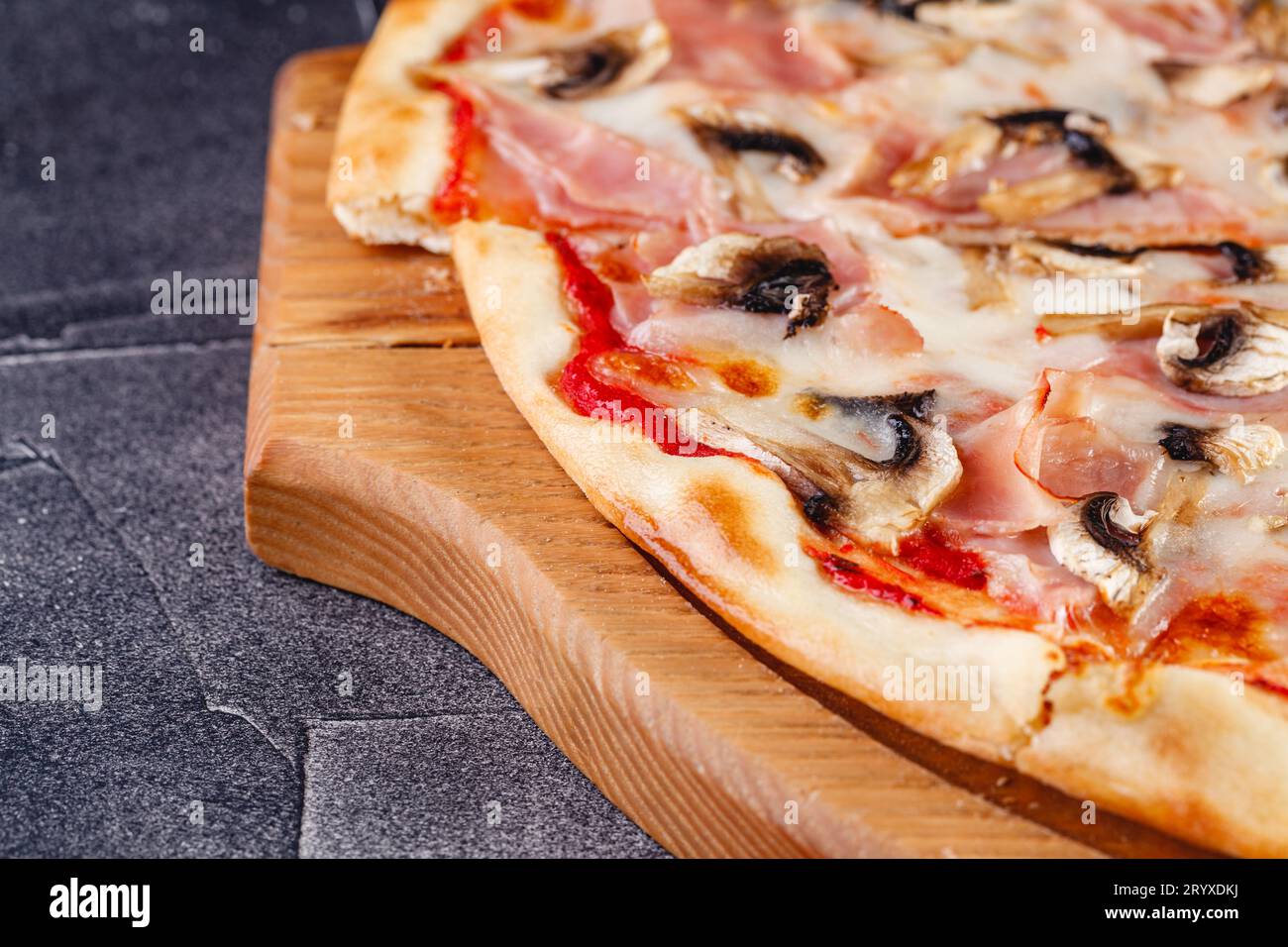 Pizza con prosciutto e funghi su tavola di legno su sfondo scuro. Primo piano Foto Stock