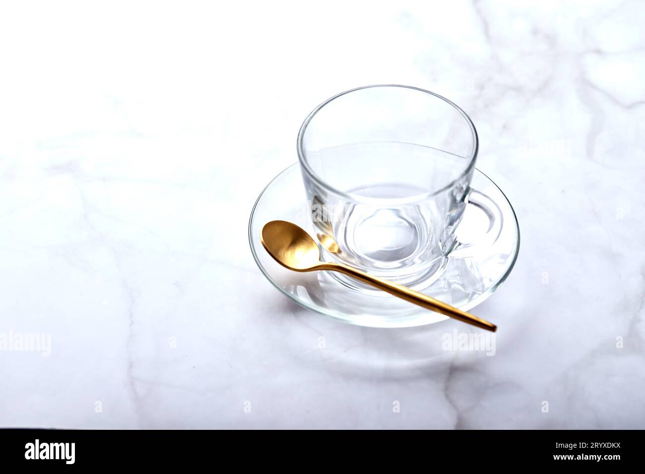 Svuotare la tazza di vetro sul piattino con il cucchiaio dorato su un tavolo in marmo chiaro Foto Stock