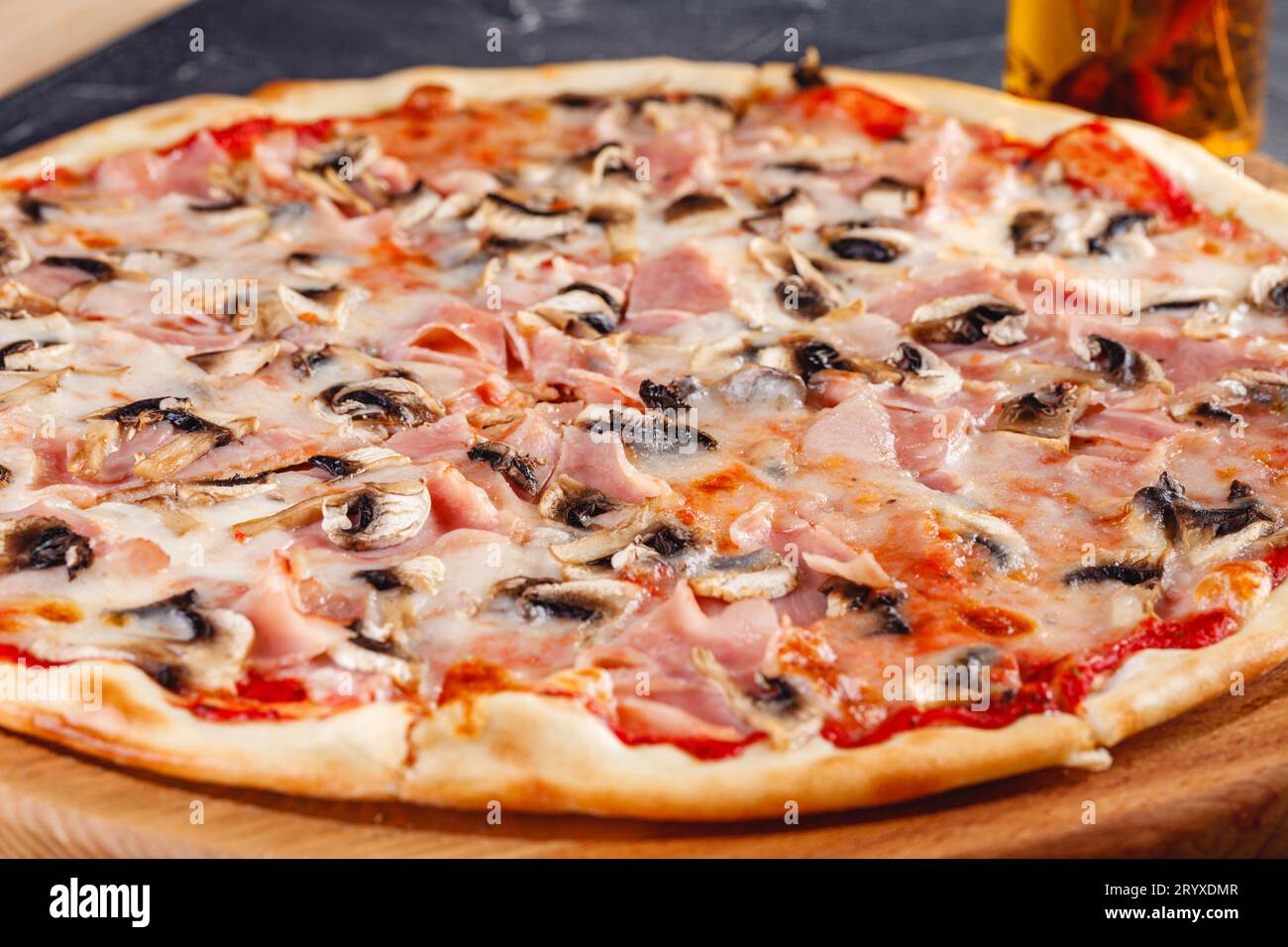 Pizza con prosciutto e funghi su tavola di legno su sfondo scuro. Primo piano Foto Stock