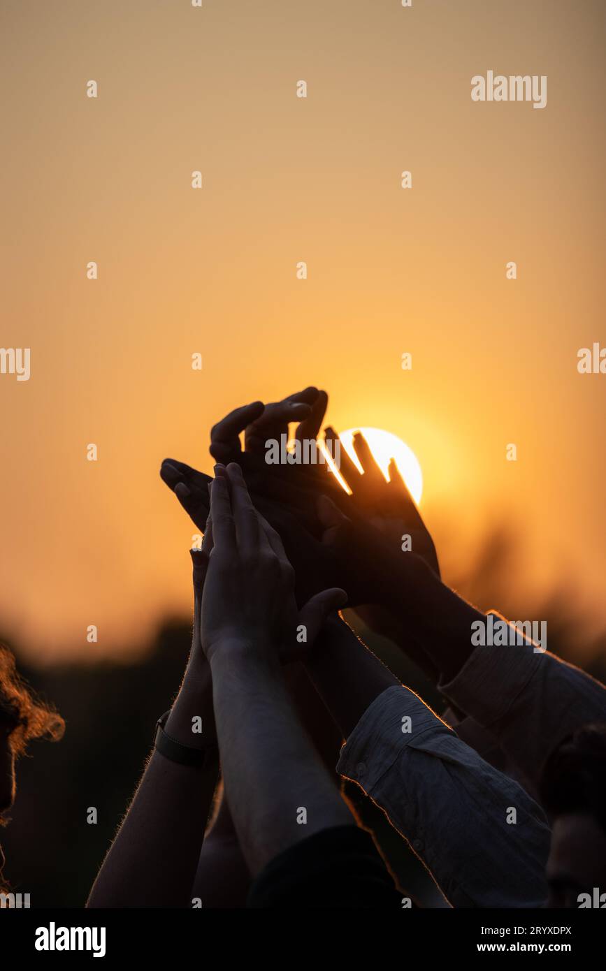 Gruppo multirazziale di giovani che danno cinque in alto contro un sole che tramonta, si sente entusiasta di concentrarsi da vicino sulle palme impilate Foto Stock