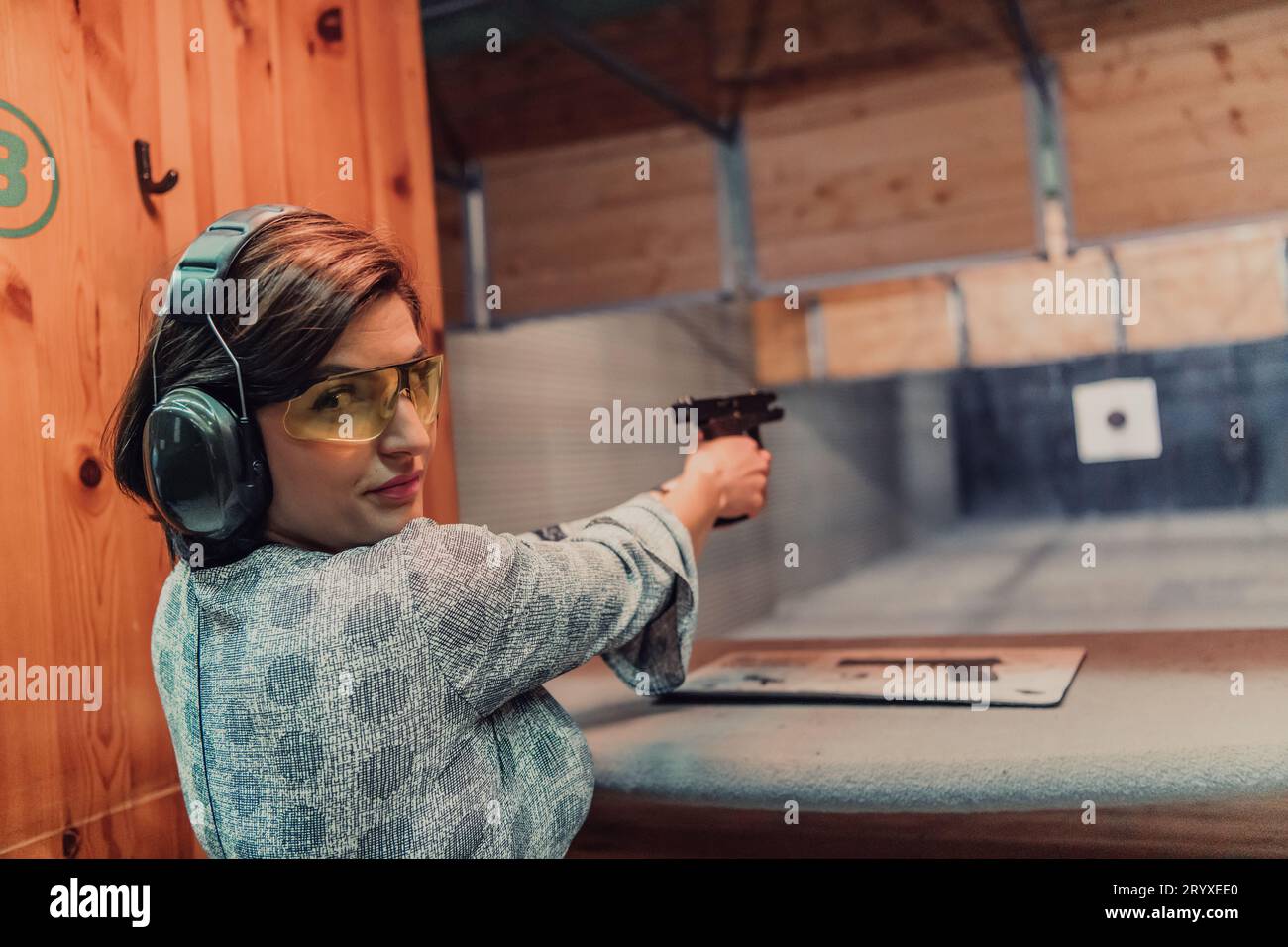 Una donna pratica a sparare a una pistola in un poligono mentre indossa cuffie protettive Foto Stock