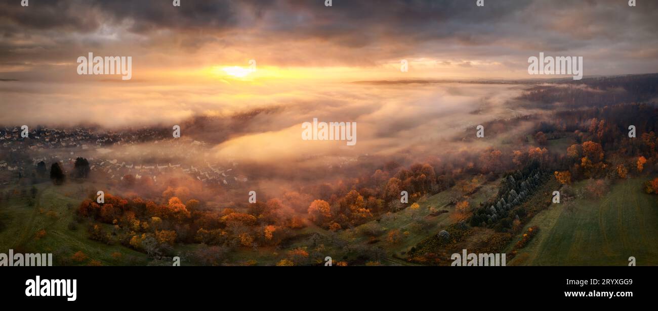 Panorama altamente suggestivo all'alba dall'alto della nebbia. Vista aerea panoramica di un bellissimo paesaggio con una magnifica luce rossa che illumina le nuvole scure Foto Stock