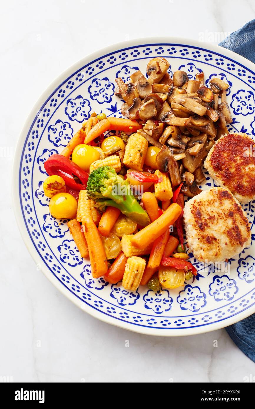 Piatto con verdure fritte, carote, broccoli, baby corn, peperoni, champagne arrosto e due palle di pollo Foto Stock