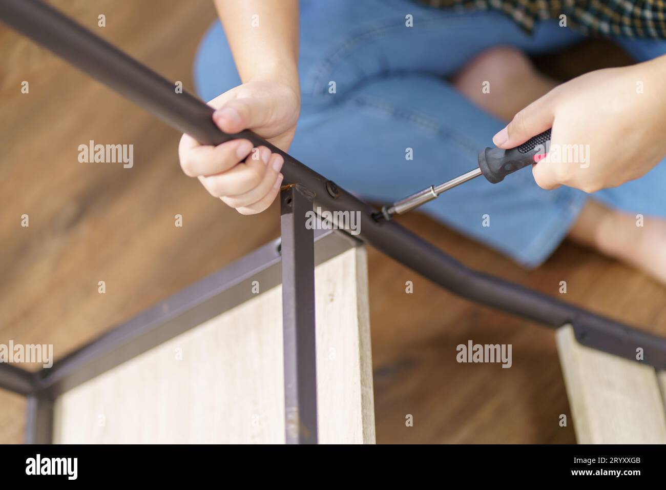 La donna asiatica ripara autonomamente i mobili rinnovati utilizzando attrezzature per riparare i mobili da casa, seduti sul pavimento. Foto Stock