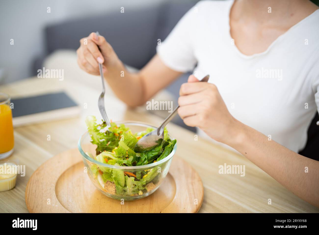 Felice bella donna asiatica che mangia cibo sano con insalata vegana in cucina a casa Foto Stock