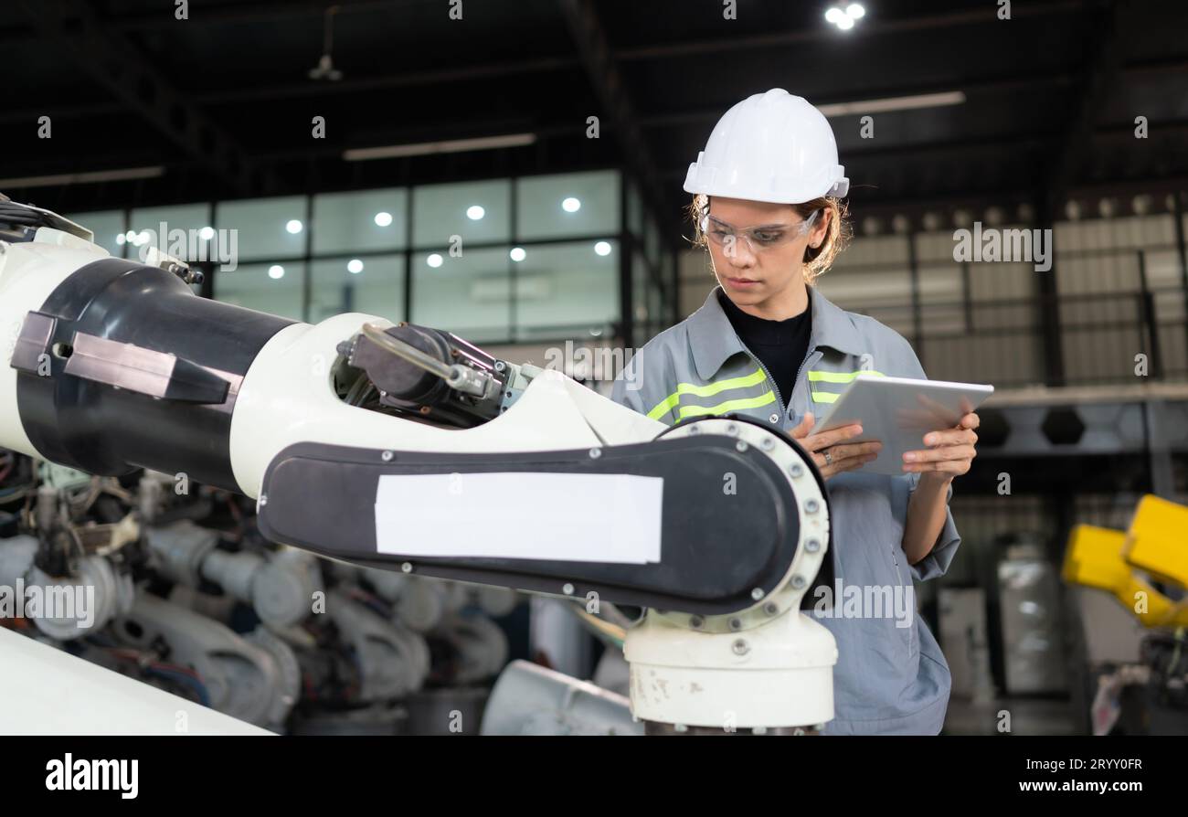 Un ingegnere donna installa un programma su un braccio robotico in un magazzino robot. E provare il funzionamento prima di inviare la macchina Foto Stock