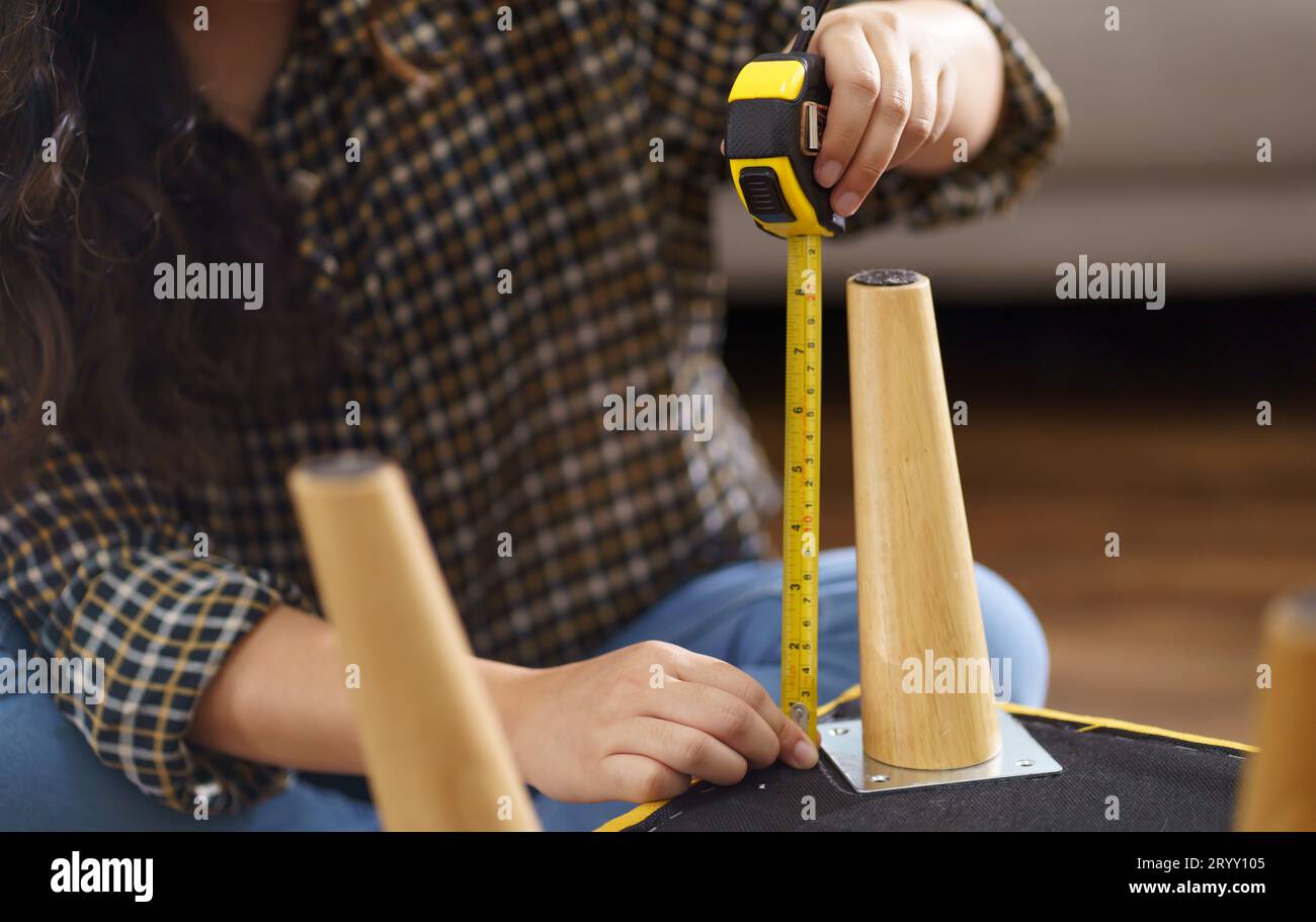 La donna asiatica ripara autonomamente i mobili rinnovati utilizzando attrezzature per riparare i mobili da casa, seduti sul pavimento Foto Stock