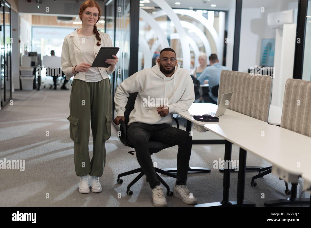 In un ufficio moderno, il giovane uomo d'affari afroamericano e la sua collega donna d'affari, con i suoi sorprendenti capelli arancioni, si impegnano Foto Stock
