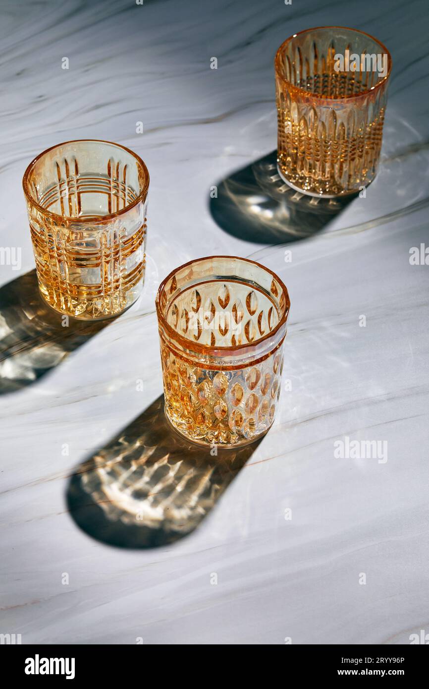 Tre bicchieri di vetro vuoti su sfondo chiaro con ombre dalla luce del sole Foto Stock