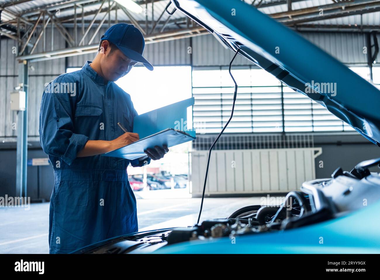 Meccanico dell'auto che tiene un appunti e controlla il veicolo di manutenzione tramite ordine di richiesta di rimborso del cliente presso l'officina di riparazione auto. Motore re Foto Stock