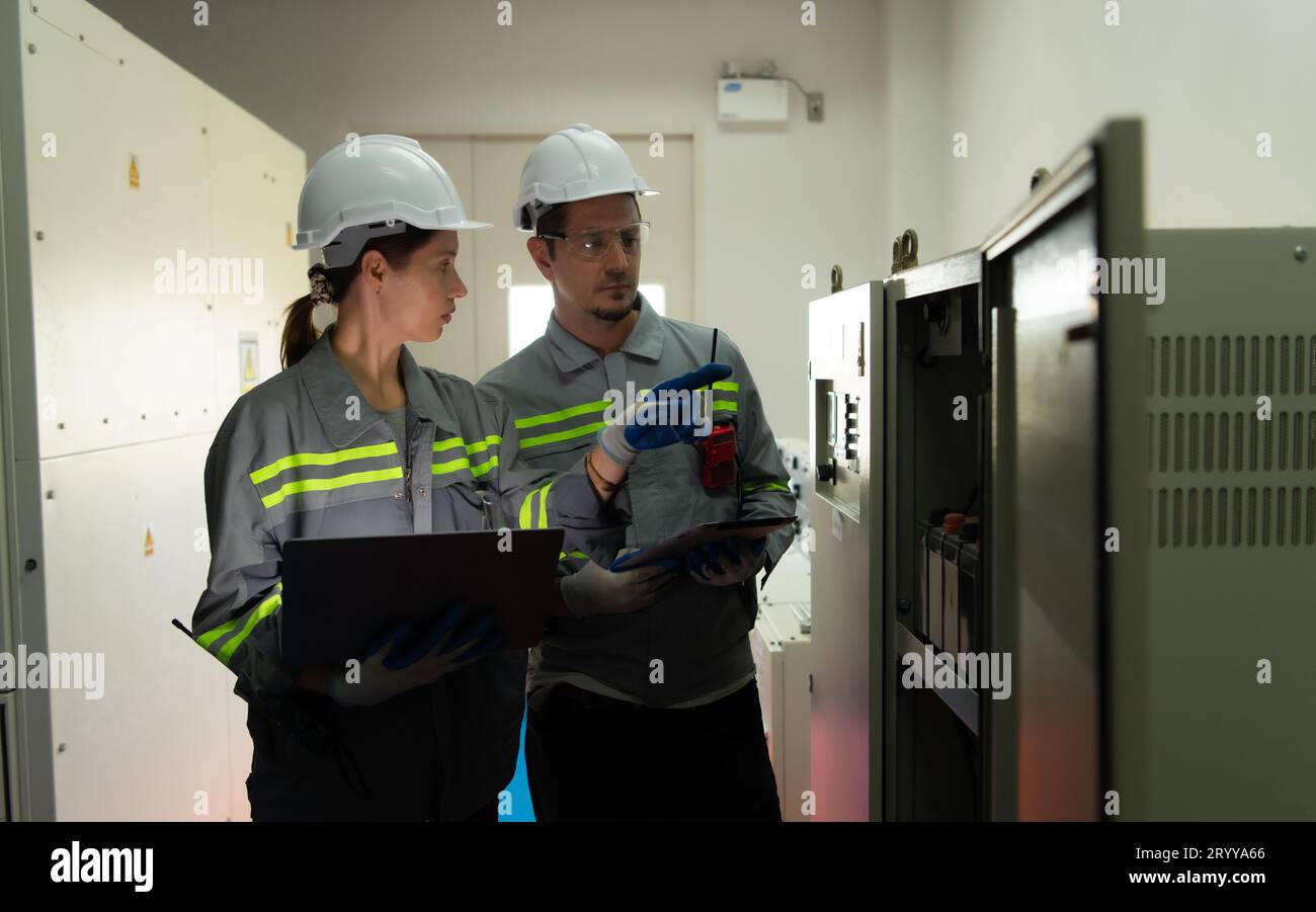 Team di ingegneri dell'energia elettrica che ispeziona il sistema di una grande stazione di stoccaggio dell'energia solare nel mezzo del campo delle celle solari in un'area di hund Foto Stock